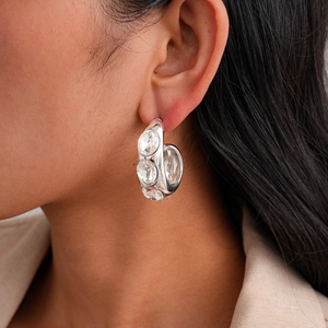 Close-up of silver geometric hoop earrings with three clear zircons on model