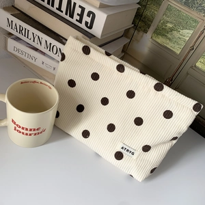 Detailed view of cream corduroy cosmetic bag with brown polka dots on a desk