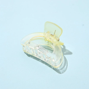 Detailed view of a transparent light yellow acetate hair claw clip on light blue surface