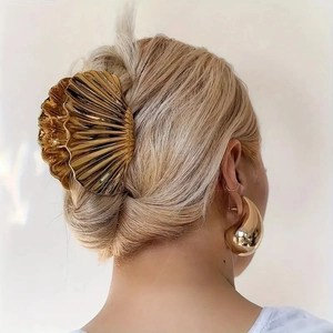 Golden shell-shaped metal hair claw clip securing a bun on blonde hair in a beach style
