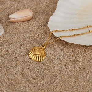 Detailed close-up of golden shell pendant on a beaded chain over a sandy beach backdrop