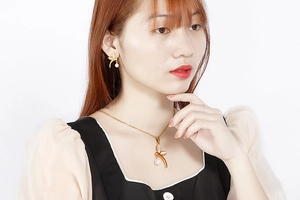 Detail view of model wearing gold leaf-shaped earrings and necklace with white pearls