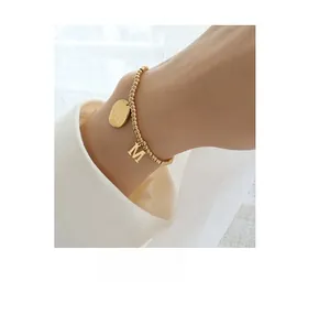 Close-up of minimalist 18k gold plated beaded bracelet with oval tag and M letter charm