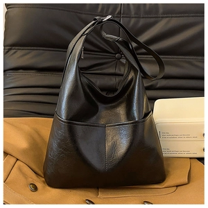 Détail du sac cabas noir montrant la texture du cuir PU brillant sur un canapé en cuir chic
