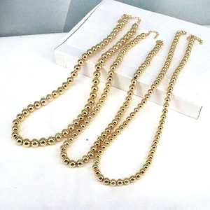 Five assorted sizes of polished gold beaded ball necklaces on a minimalist white stand
