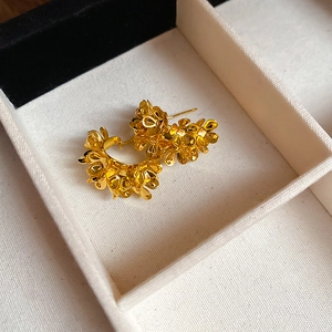 Elegant golden floral C-shape earrings in a jewelry box featuring intricate petal designs