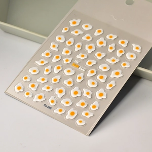 Macro shot of 3D embossed fried egg nail stickers with glossy orange yolks and white texture