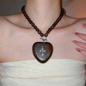 Détail d'un collier en perles de bois avec pendentif cœur et croix en métal
