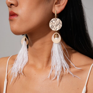 Close-up of white feather tassel earrings with gold metal rings worn by a model