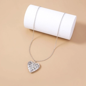 Dettaglio di un ciondolo a cuore in argento traforato su un supporto bianco cilindrico