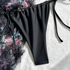 Detail of glossy black bikini bottoms with drawstring and floral mesh cover-up skirt