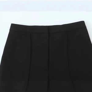 Women's black casual stirrup pants showing detailed waist stitching and front fly