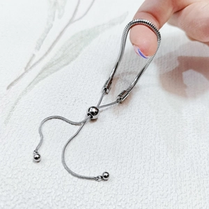 Detail of adjustable silver snake chain bracelet with sliding ball clasp and tassel charms