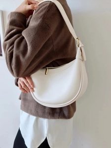 White leather crescent moon bag with gold zipper shown on model's shoulder