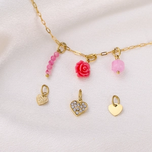 Detail of gold necklace with pink charms and textured heart pendants on white silk