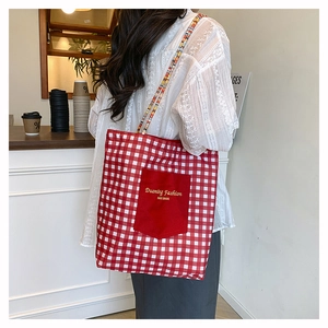 Detalle de bolso tote de lona a cuadros rojos con letras bordadas amarillas en bolsillo