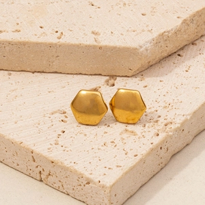 Detailed macro view of matte gold hexagonal stud earrings on textured travertine stone
