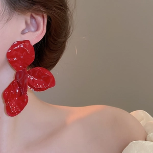 Close-up of oversized red flower earrings with glossy petals on a female model