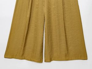 Detailed view of golden high-gloss wide-leg trousers with silky satin texture