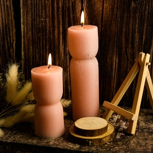 Dettaglio di candele rosa a coste geometriche accese su sfondo in legno rustico