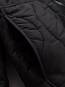 Detail of black quilted jacket showing ripstop fabric texture and side pocket design