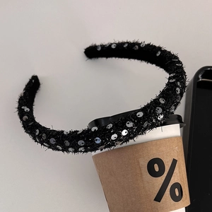 Close-up of a black plush headband with shiny silver sequins on a white coffee cup
