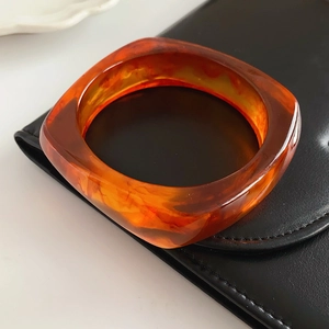 Macro shot of thick square amber resin bangle with tortoiseshell texture on black leather