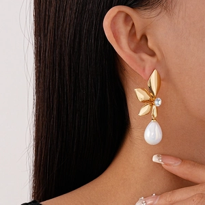Detail of golden flower earring with clear crystal and white teardrop pearl on model