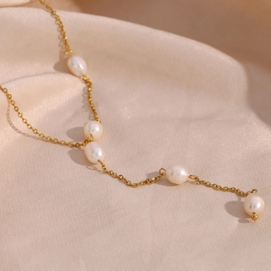 Close-up of golden Y-chain necklace with five baroque pearls on soft beige silk