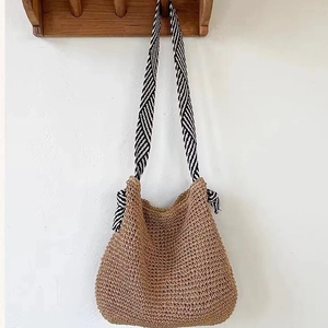 Minimalist straw shoulder bag in natural brown with a striped fabric strap hanging on a wall
