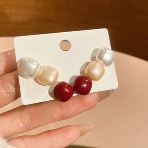Macro shot of minimalist square stud earrings in crimson and cream on a display card