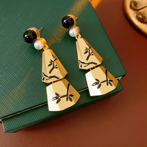 Detailed view of gold earrings with pearl tassels and bamboo carved fan pendants