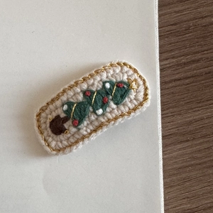 Close-up of beige knit Christmas hair clip featuring green trees with red and gold details