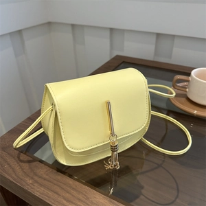 Minimalist light yellow leather saddle bag with gold tassel on a wooden table setup