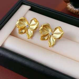 Detailed macro view of gold-tone pleated bow earrings with a sparkling center zircon