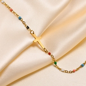 Detail view of gold stainless steel cross necklace with colorful beads on satin fabric