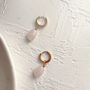 Detailed shot of gold hoop earrings with oval pink natural stone pendants on white texture