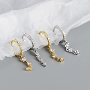 Close-up of gold and silver huggie earrings with sparkling CZ tassels on textured paper
