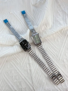 Close-up of square quartz watches with black and green dials on white fabric