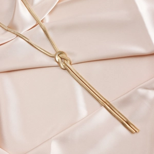 Close-up of golden snake chain lariat necklace with knot design on pink silk background