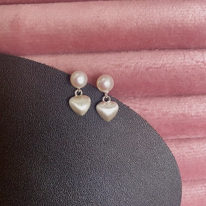 Brushed heart-shaped earrings with freshwater pearls on a pink textured display