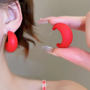 Detail of matte burgundy acrylic C-shaped earrings worn on ear showing size and texture
