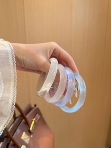 Gros plan de quatre bracelets œil de chat translucides aux couleurs pastel sur une main
