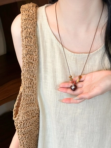 Detail of wooden bead necklace featuring a heart pendant with saturn ring logo emblem