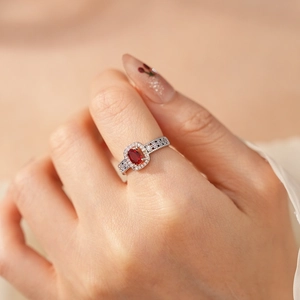 Close-up of silver halo ring with oval red gemstone and pavé diamonds for women