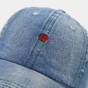 Close-up of red rose embroidery and denim texture on light blue baseball cap