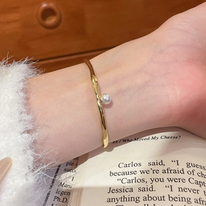 Détail du bracelet ouvert plaqué or 18k avec perle élégante sur un fond de style de vie doux