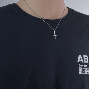 Close-up of a silver cross pendant necklace with a small diamond on a female model