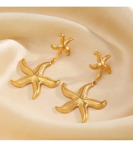 Detailed view of gold starfish drop earrings on soft beige silk textured fabric