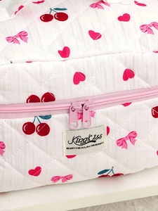 Detail of quilted white cotton makeup bag with cherry and bow patterns and pink zipper
